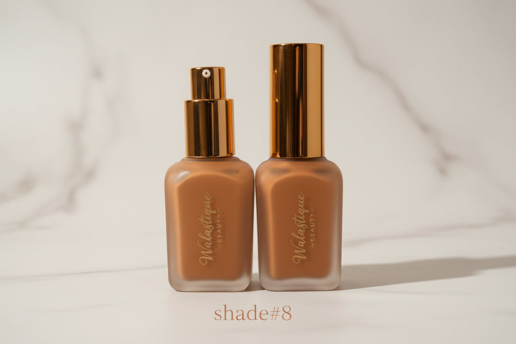 Two bottles of Walastique foundation with gold caps on a textured surface.