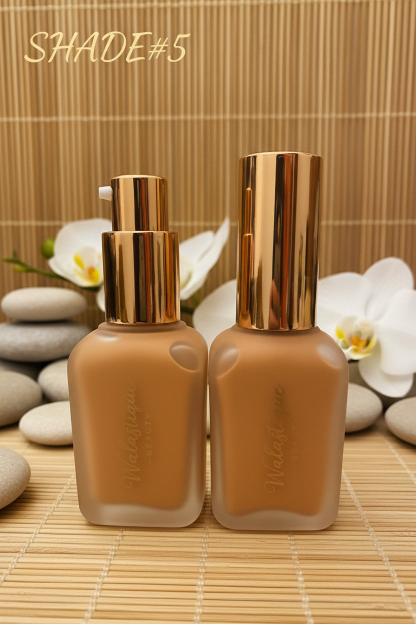 Two bottles of Walastique Beauty Liquid foundation with gold caps on a textured surface.
